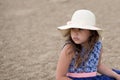 Little girl sitting in summer hat and beautiful dress on the beach Royalty Free Stock Photo