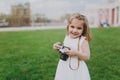 Little cute child baby girl in light dress take picture on retro vintage photo camera on green grass in park. Mother Royalty Free Stock Photo