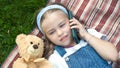 Little cute child girl laying on a blanket on green lawn in summer outdoors with her teddy bear toy talking on mobile phone Royalty Free Stock Photo