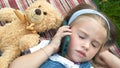 Little cute child girl laying on a blanket on green lawn in summer outdoors with her teddy bear toy talking on mobile phone Royalty Free Stock Photo