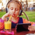 Little cute child girl wearing headphones listens online web free audio course outdoors, female kid using mobile phone for e- Royalty Free Stock Photo