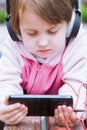 Little cute child girl wearing headphones listens online web free audio course outdoors, female kid using mobile phone for e- Royalty Free Stock Photo