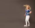 Little cute child kid blonde girl 7-8 years old wearing bright summer clothes dancing on black wall background, children studio Royalty Free Stock Photo