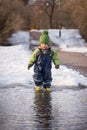 Little cute child in rubber boots running into the puddle and having fun in the spring park. Boy jumping Royalty Free Stock Photo