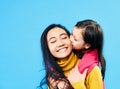 Little cute daughter hug and kissing her happy mother isolated on blue background Royalty Free Stock Photo