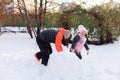 Little cute daughter with mother making big snow balls for building snowman on backyard in evening with rowan and fir Royalty Free Stock Photo