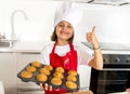 Little and cute girl alone in cook hat and apron presenting and showing tray with muffins smiling happy