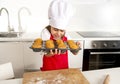 Little and cute girl alone in cook hat and apron presenting and showing tray with muffins smiling happy