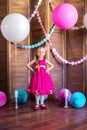 Little cute girl with blond hair in a pink dress and a princess crown with large bright balloons and garlands. Children`s holiday.