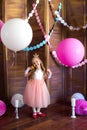 Little cute girl with blond hair in a pink dress and a princess crown with large bright balloons and garlands. Children`s holiday.