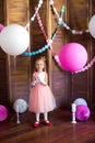 Little cute girl with blond hair in a pink dress and a princess crown with large bright balloons and garlands. Children`s holiday.