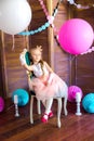 Little cute girl with blond hair in a pink dress and a princess crown with large bright balloons and garlands. Children`s holiday.