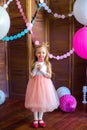 Little cute girl with blond hair in a pink dress and a princess crown with large bright balloons and garlands. Children`s holiday.