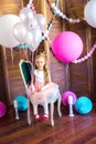 Little cute girl with blond hair in a pink dress and a princess crown with large bright balloons and garlands. Children`s holiday.