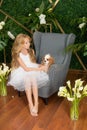 Little cute girl with blond hair in a white dress holding a small dog and white flowers, lilies and orchids Royalty Free Stock Photo