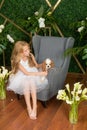 Little cute girl with blond hair in a white dress holding a small dog and white flowers, lilies and orchids Royalty Free Stock Photo