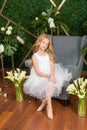 Little cute girl with blond hair in a white dress and white flowers, lilies and orchids Royalty Free Stock Photo