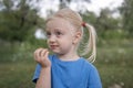 Little cute girl with blonde hair gathered in ponytails with green apple in hand. Child in summer garden, spends time in nature Royalty Free Stock Photo