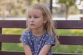 Little cute girl blonde six years old sits in the park on a bench and dreams, Royalty Free Stock Photo