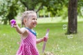 A little cute girl in a colorful dress blowing soap bubbles in summer park. Royalty Free Stock Photo