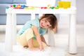 Little cute girl crawled under the table. The kid smiles, plays hide and seek Royalty Free Stock Photo