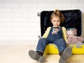 Little cute girl in denim overalls and boots. sits with his friend a teddy bear in an opened suitcase. Ready to travel.