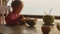 Little cute girl eating coconut by spoon at cafe with seaview
