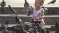 Little cute girl feeds pigeons near fountain