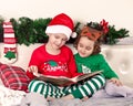 Little cute girl in funny deer mask and boy in Santa cap and Christmas pajamas reading a book. Royalty Free Stock Photo