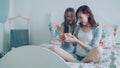 Little cute girl giving gift box to her young happy mother celebrating birthday sitting on bed in cozy bedroom at home Royalty Free Stock Photo