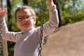 Little cute girl in glasses smiling rides on a swing at the playground in the park