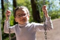 Little cute girl in glasses smiling rides on a swing at the playground in the park