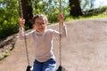 Little cute girl in glasses smiling rides on a swing at the playground in the park