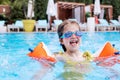 Little cute girl in goggles, yellow swimsuit and orange inflatable armlets swiming in pool hotel Royalty Free Stock Photo