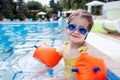 Little cute girl in goggles, yellow swimsuit and orange inflatable armlets swiming in pool hotel Royalty Free Stock Photo