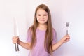 Little cute girl holding a knife and fork, with a satisfied expression on her face, on a light background