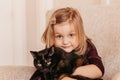 A little cute girl holds a black cat in her arms. Girl at home with her pet. Little girl loves her cute kitten Royalty Free Stock Photo