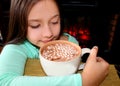 Little cute girl with hot chocolate by the fireplace.