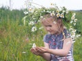 Little cute girl in a huge wreath of chamomile