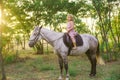 Little cute girl with light curly hair in a straw hat riding a horse at sunset Royalty Free Stock Photo