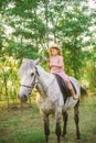 Little cute girl with light curly hair in a straw hat riding a horse at sunset Royalty Free Stock Photo