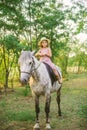 Little cute girl with light curly hair in a straw hat riding a horse at sunset Royalty Free Stock Photo