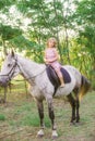 Little cute girl with light curly hair in a straw hat riding a horse at sunset Royalty Free Stock Photo