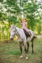 Little cute girl with light curly hair in a straw hat riding a horse at sunset Royalty Free Stock Photo