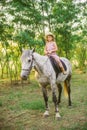 Little cute girl with light curly hair in a straw hat riding a horse at sunset Royalty Free Stock Photo