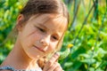 Little cute girl with a long braid, eating a cucumber plucked from the garden