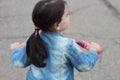 A little cute girl with long dark hair in a denim suit sits on a pink bicycle. Gray blurred asphalt in the background