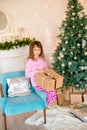 Little cute girl in pajamas near a Christmas tree with gifts and a bright fireplace decorated with garlands, needles and candles. Royalty Free Stock Photo