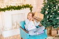 Little cute girl in pajamas near a Christmas tree with gifts and a bright fireplace decorated with garlands, needles and candles. Royalty Free Stock Photo