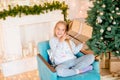 Little cute girl in pajamas near a Christmas tree with gifts and a bright fireplace decorated with garlands, needles and candles. Royalty Free Stock Photo